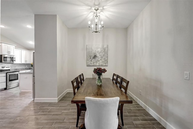 dining room featuring an inviting chandelier, baseboards, lofted ceiling, and wood finish floors