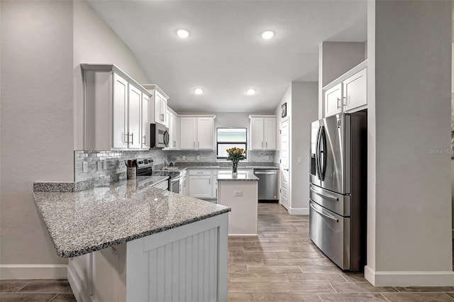 kitchen with appliances with stainless steel finishes, kitchen peninsula, decorative backsplash, white cabinetry, and stone counters