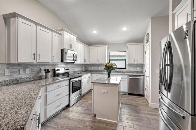 kitchen featuring wood finish floors, stainless steel appliances, a kitchen island, and backsplash