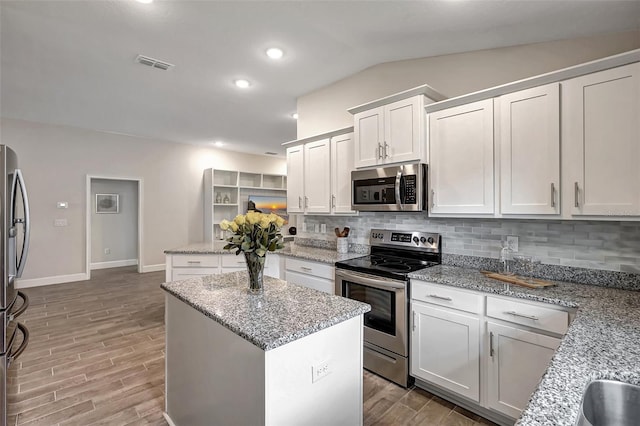 kitchen featuring white cabinets, a center island, hardwood / wood-style floors, appliances with stainless steel finishes, and decorative backsplash