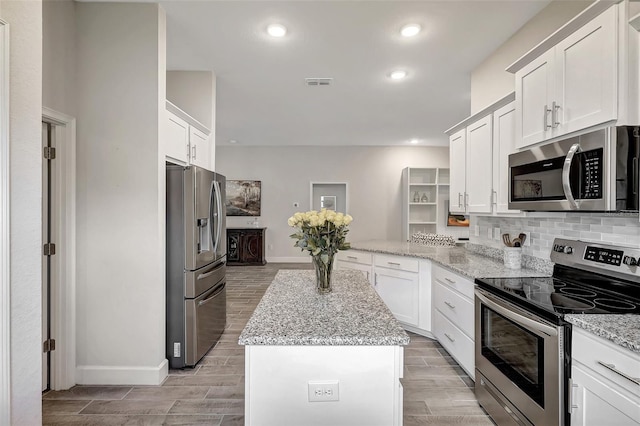 kitchen with white cabinets, light stone counters, stainless steel appliances, and light hardwood / wood-style floors