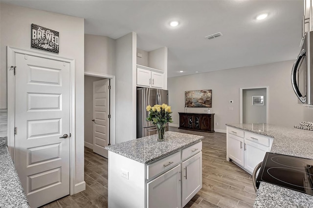 kitchen with visible vents, black range with electric cooktop, wood tiled floor, freestanding refrigerator, and white cabinets