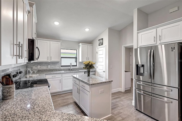 kitchen featuring vaulted ceiling, white cabinetry, light hardwood / wood-style flooring, and stainless steel appliances