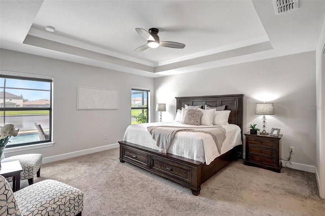 carpeted bedroom featuring a tray ceiling, multiple windows, and ceiling fan