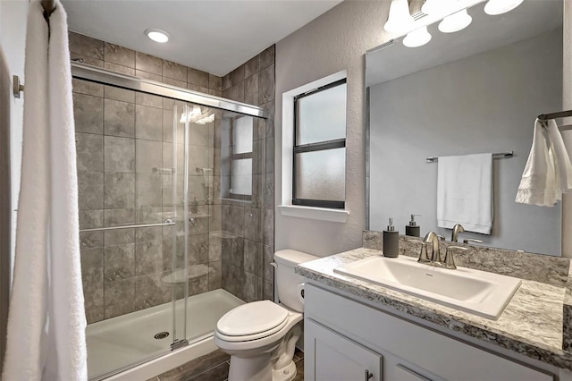 bathroom with toilet, a shower with door, and vanity