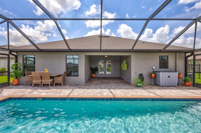 rear view of house with a shingled roof, a lanai, a patio area, and stucco siding