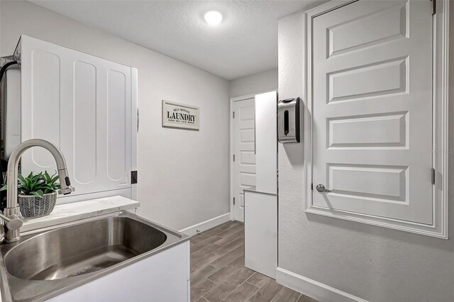 interior space with a textured ceiling, sink, white cabinets, and light hardwood / wood-style floors