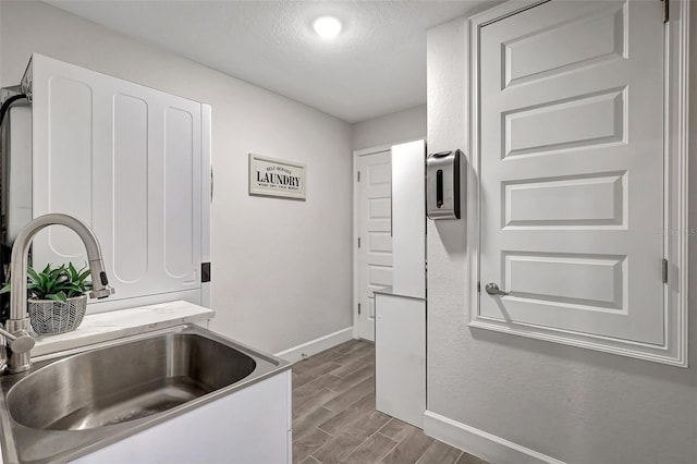 kitchen with baseboards, wood finish floors, a sink, light countertops, and a textured ceiling