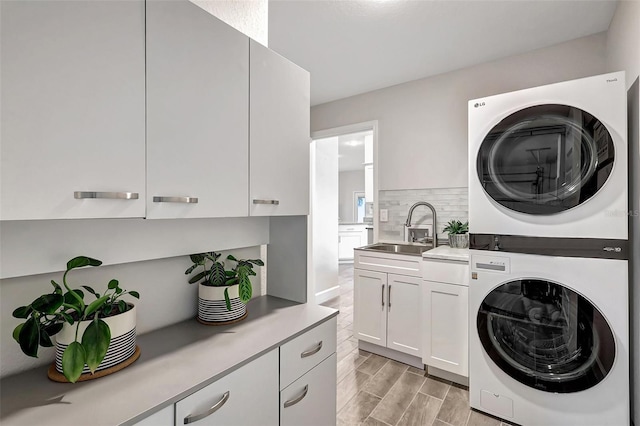 laundry room featuring wood finish floors, stacked washer and dryer, cabinet space, and a sink