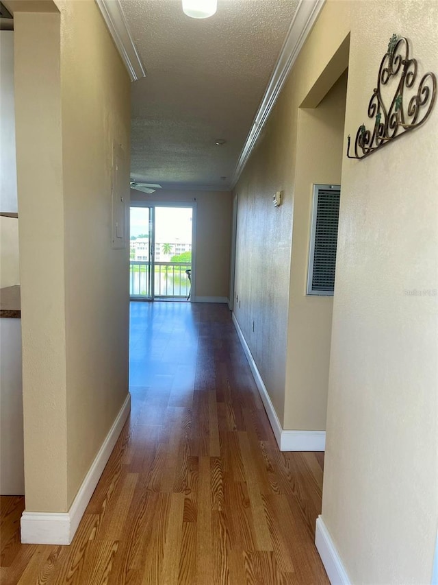 hall with wood finished floors, a textured ceiling, crown molding, and baseboards