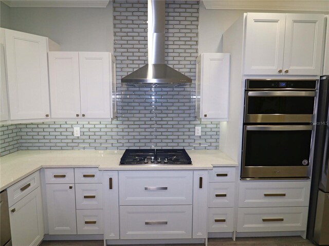 kitchen with appliances with stainless steel finishes, wall chimney exhaust hood, white cabinets, and decorative backsplash