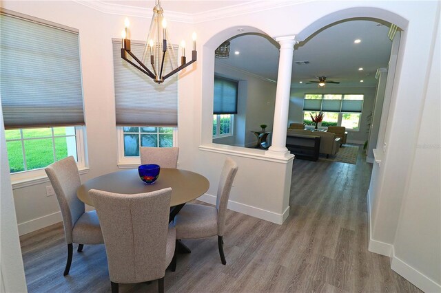 dining space featuring hardwood / wood-style flooring, ornamental molding, ceiling fan with notable chandelier, and decorative columns