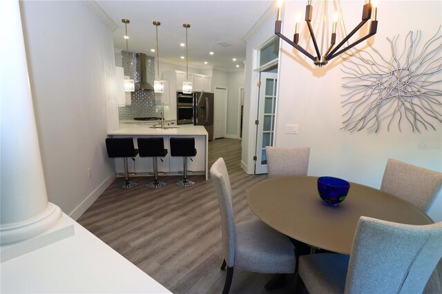 dining room featuring crown molding, a notable chandelier, hardwood / wood-style floors, and decorative columns