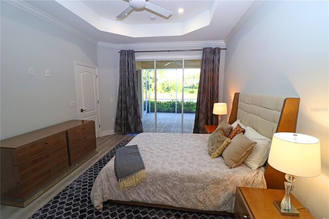 bedroom with a raised ceiling, wood-type flooring, crown molding, access to exterior, and ceiling fan