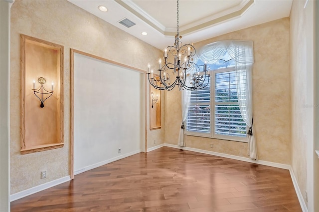 unfurnished dining area featuring a tray ceiling, ornamental molding, a chandelier, and hardwood / wood-style flooring