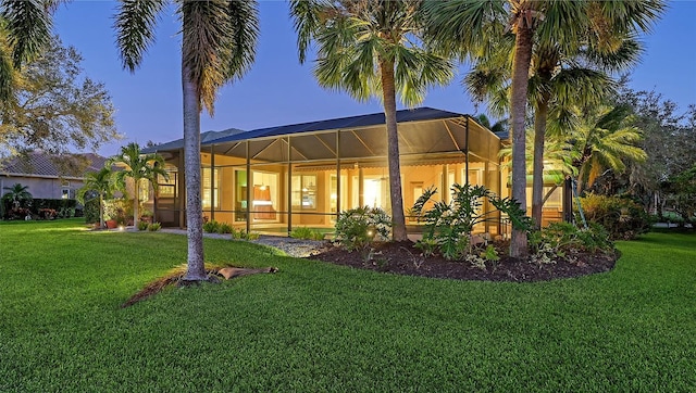 back house at dusk featuring a lanai and a yard