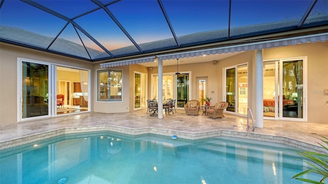 pool at dusk featuring glass enclosure, ceiling fan, and a patio