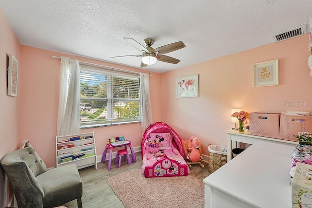 recreation room featuring ceiling fan, light hardwood / wood-style floors, and a textured ceiling