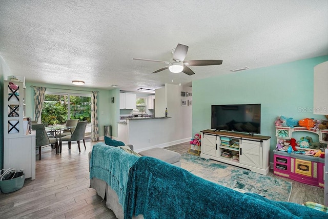 living room featuring ceiling fan, a textured ceiling, and light hardwood / wood-style flooring