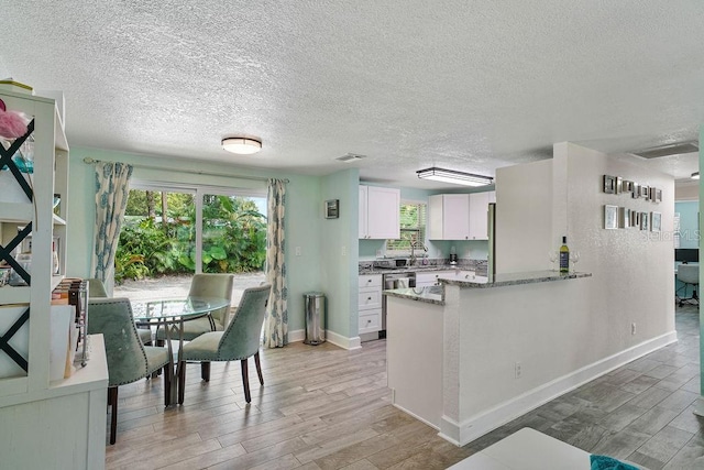 kitchen with light stone counters, wood-type flooring, kitchen peninsula, and white cabinets