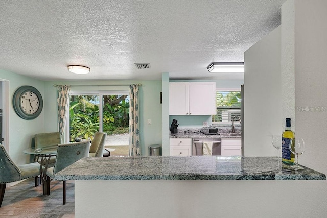 kitchen featuring stone counters, white cabinets, stainless steel dishwasher, kitchen peninsula, and light wood-type flooring