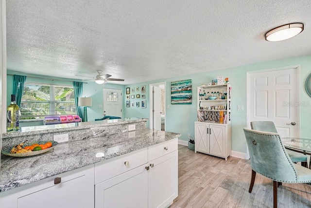 kitchen featuring light stone counters, a textured ceiling, white cabinets, and light wood-type flooring