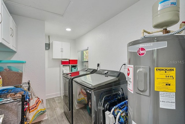 clothes washing area with cabinets, electric water heater, washer and clothes dryer, and light hardwood / wood-style flooring