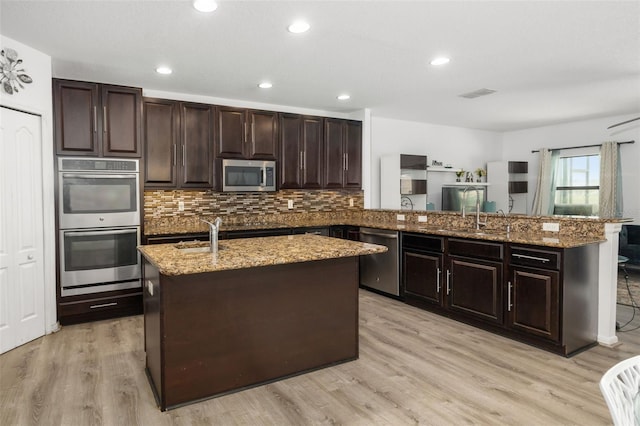 kitchen with light hardwood / wood-style floors, appliances with stainless steel finishes, a center island with sink, and kitchen peninsula