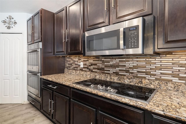 kitchen featuring appliances with stainless steel finishes, light stone countertops, dark brown cabinetry, and light hardwood / wood-style flooring