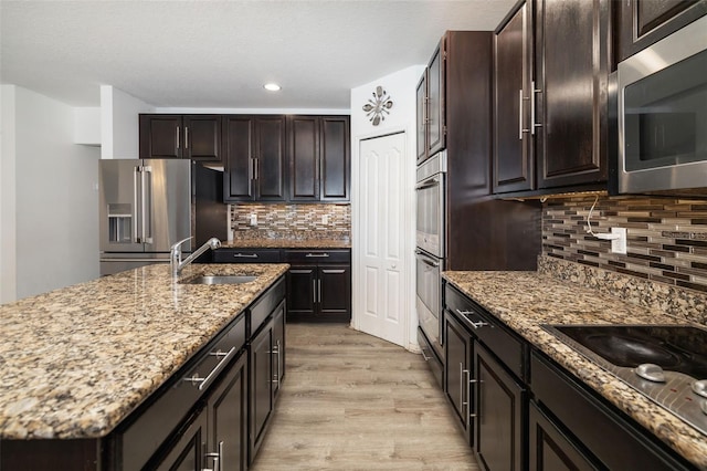 kitchen featuring backsplash, light wood-type flooring, appliances with stainless steel finishes, sink, and a kitchen island with sink