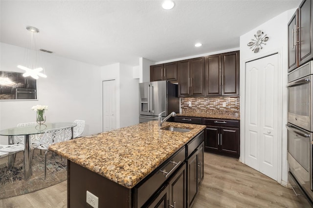 kitchen featuring light hardwood / wood-style flooring, decorative light fixtures, stainless steel appliances, sink, and a center island with sink