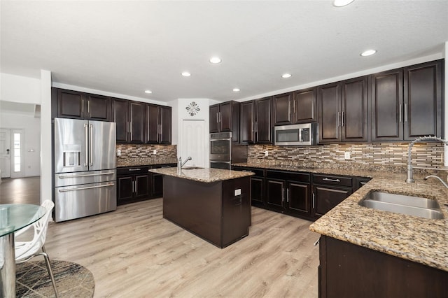 kitchen featuring a kitchen island, dark brown cabinets, stainless steel appliances, sink, and light wood-type flooring