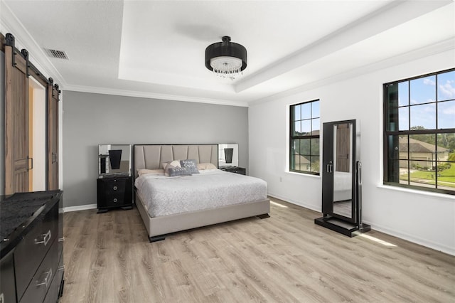 bedroom featuring crown molding, a barn door, a raised ceiling, and light wood-type flooring