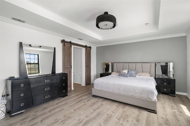 bedroom featuring ornamental molding, light wood-type flooring, a tray ceiling, and a barn door