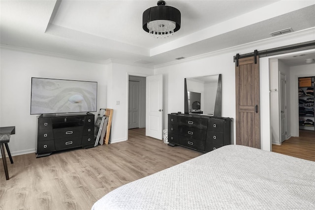 bedroom featuring a barn door, a tray ceiling, light wood-type flooring, and ornamental molding