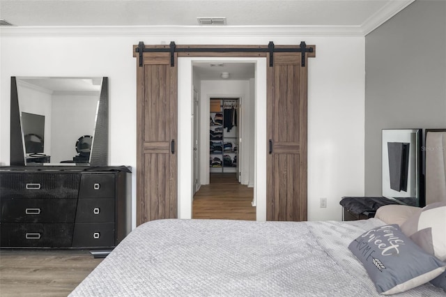 bedroom with a barn door, ornamental molding, and wood-type flooring