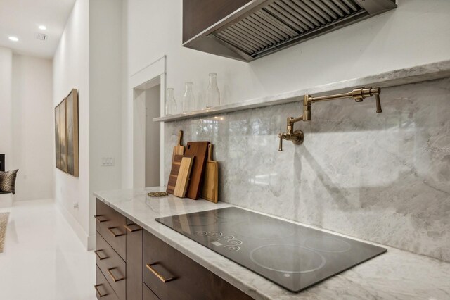 kitchen featuring light stone counters, black electric cooktop, and custom range hood