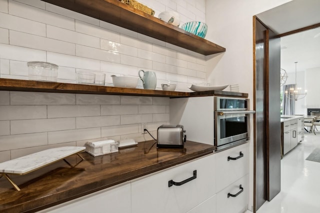 details with oven, an inviting chandelier, white cabinets, and decorative backsplash