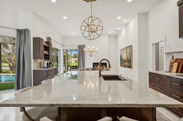 kitchen with pendant lighting, light stone counters, an inviting chandelier, sink, and dark brown cabinetry