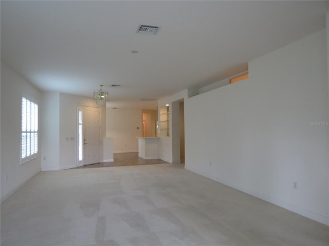 unfurnished living room with visible vents, light carpet, and an inviting chandelier