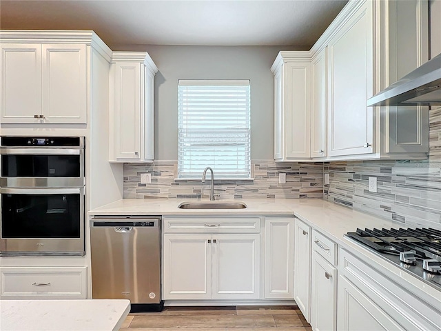 kitchen with light hardwood / wood-style floors, sink, white cabinetry, wall chimney range hood, and appliances with stainless steel finishes