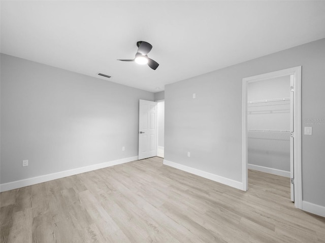 unfurnished bedroom with ceiling fan, a walk in closet, a closet, and light wood-type flooring