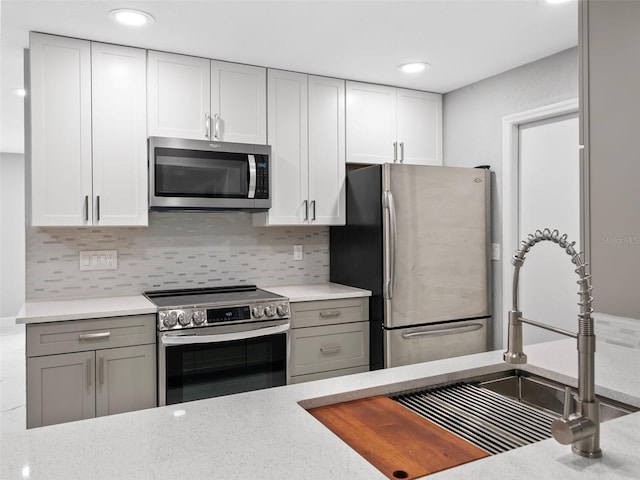 kitchen featuring tasteful backsplash, sink, appliances with stainless steel finishes, gray cabinetry, and light stone counters