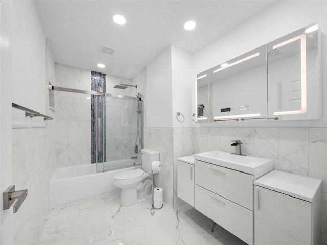 full bathroom featuring toilet, bath / shower combo with glass door, tile walls, and vanity