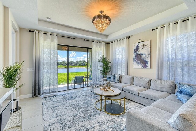 tiled living room with a notable chandelier, a water view, a tray ceiling, and a textured ceiling