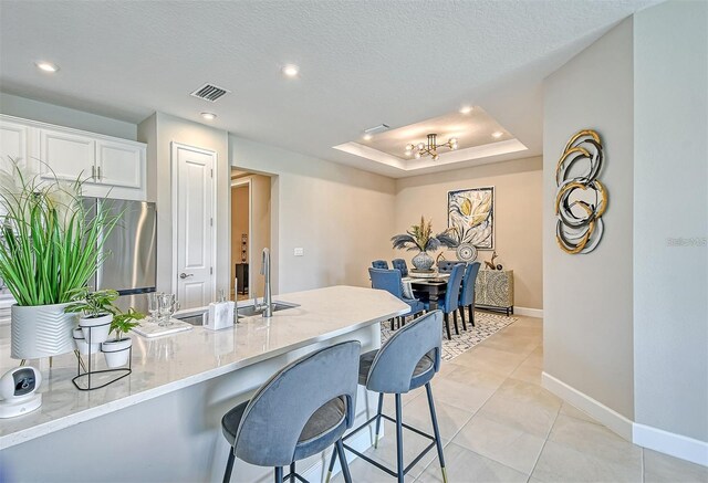 kitchen featuring a breakfast bar, a textured ceiling, white cabinetry, a raised ceiling, and light tile patterned floors