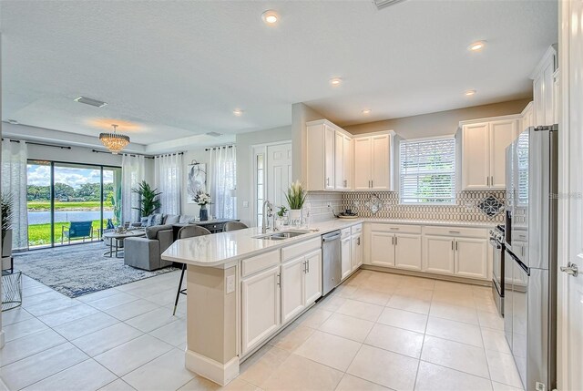 kitchen featuring appliances with stainless steel finishes, white cabinets, kitchen peninsula, light tile patterned floors, and sink