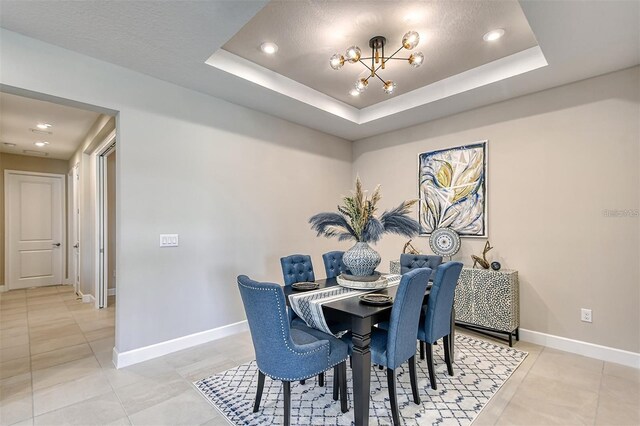 dining area with light tile patterned flooring, a tray ceiling, and a textured ceiling