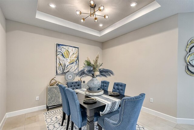 dining area featuring a notable chandelier, a raised ceiling, and light tile patterned flooring