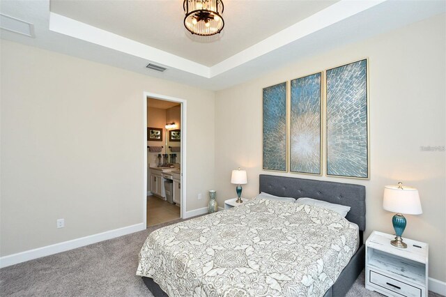 carpeted bedroom with a tray ceiling and ensuite bathroom